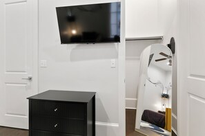 A room with a flat-screen TV mounted on the wall, a black dresser with drawers, and a large mirror with a decorative frame.