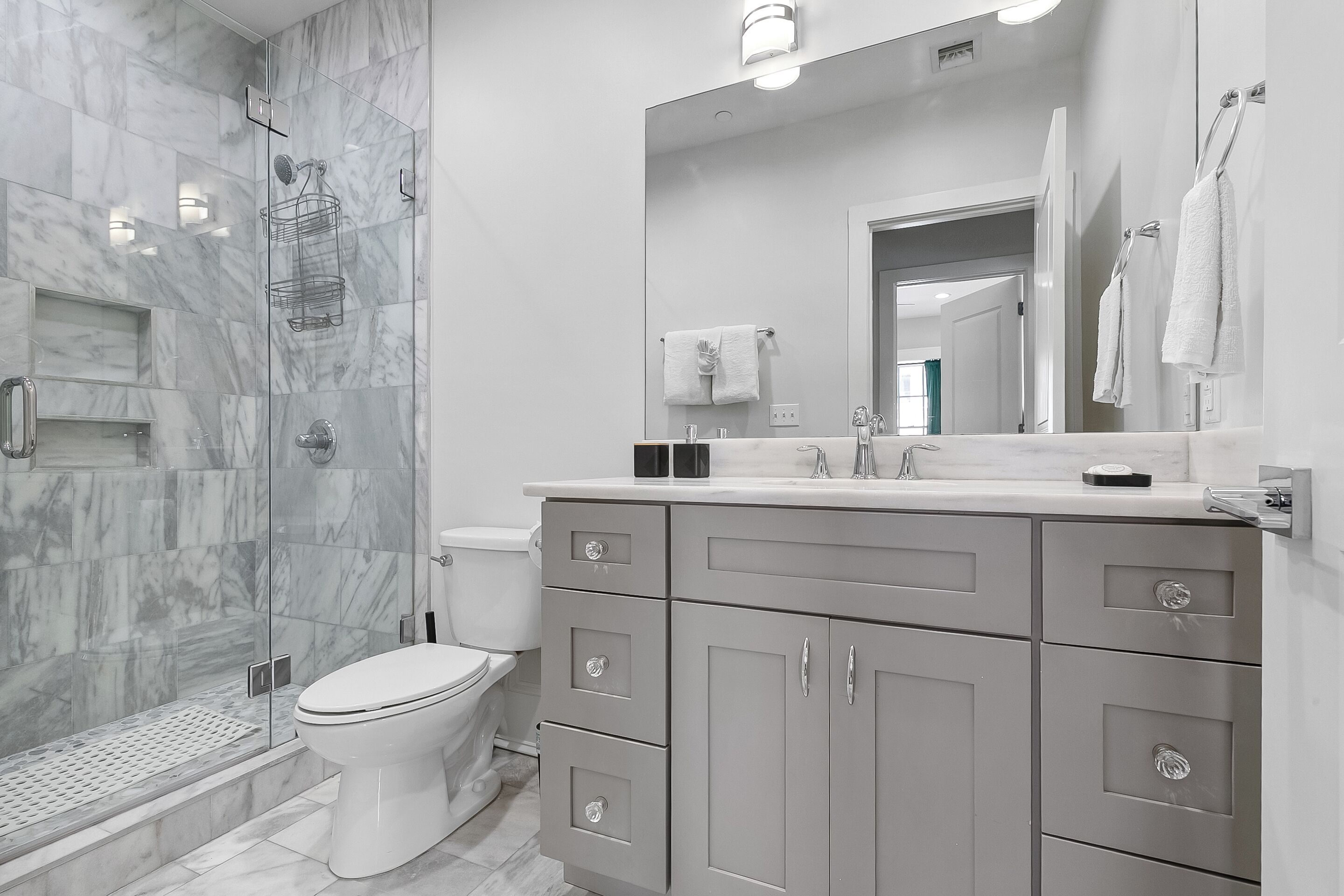 Un baño moderno con cabina de ducha de vidrio, inodoro y tocador con cajones y espejo.