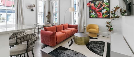 Una sala de estar moderna con un sofá, sillas, un comedor y un ventanal grande.