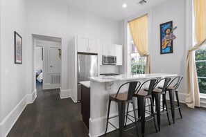 A modern kitchen with white cabinets, a stainless steel refrigerator, a microwave, and a bar area with stools.