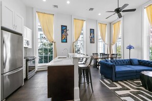 Cocina moderna con una isla central, comedor con sofá azul y obras de arte en las paredes.