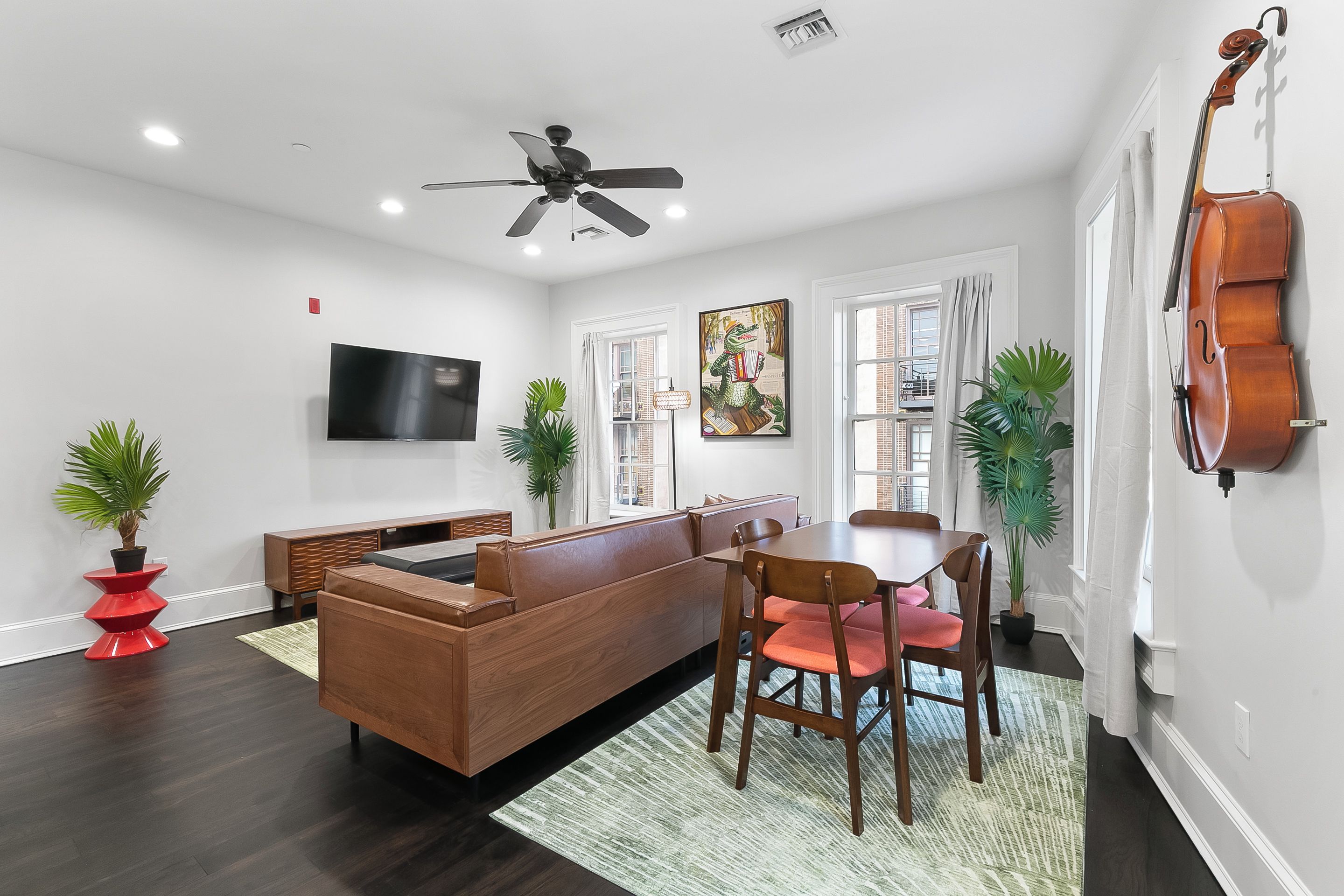 Un salon moderne comprenant un canapé, une table à manger, des chaises, un ventilateur de plafond, un téléviseur à écran plat et un violon accroché au mur.