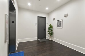 A hallway with a dark wood floor, a potted plant, a door marked '3A', and a wall-mounted light fixture. - The Melody  (New Orleans)