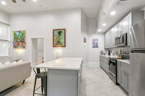 A modern kitchen with stainless steel appliances, a marble island, and artwork on the walls. - The Melody  (New Orleans)