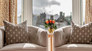 Ein Zimmer mit zwei Sofas, einer Blumenvase und Blick auf eine Stadtkulisse durch große Fenster.
