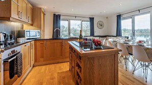 A modern kitchen with wooden cabinets, a microwave, and a dining area with a view of a lake. - 4 Bed in Newport (oc-94556) (Whippingham)