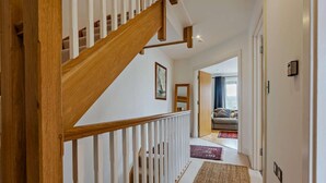A wooden staircase with white railings leading to a living area with a sofa and a view of the outdoors. - 4 Bed in Newport (oc-94556) (Whippingham)