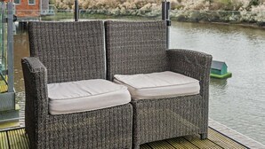 A wicker chair with cushions on a deck overlooking a body of water. - 4 Bed in Newport (oc-94556) (Whippingham)