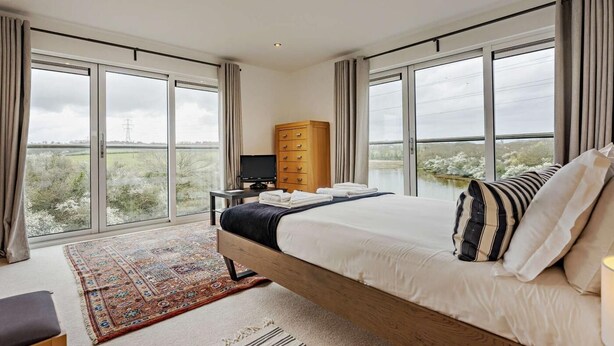 A bedroom with a large bed, a TV, a wooden dresser, and a view of the countryside. - 4 Bed in Newport (oc-94556) (Whippingham)