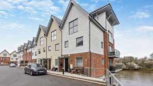 A row of modern apartment buildings with a flat roof, a paved driveway, and a body of water in the background. - 4 Bed in Newport (oc-94556) (Whippingham)