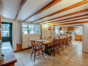 A dining area with a wooden table and chairs, a window with a view, and a kitchen in the background. - 6 Bed in Filey (oc-94524) (Reighton Gap)
