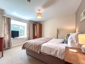 A bedroom with a bed, a bedside table, a mirror, a wardrobe, and a window with curtains. - 6 Bed in Filey (oc-94524) (Reighton Gap)