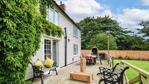Een terras met tuinmeubilair, een bakoven en een wit gebouw met groene beplanting.