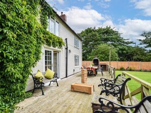 A patio with outdoor furniture, a brick oven, and a white building with green foliage. - 6 Bed in Filey (oc-94524) (Reighton Gap)