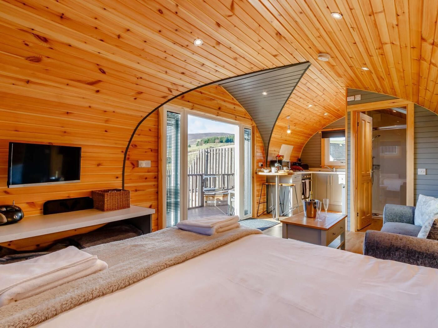 A cozy cabin interior with a bed, a desk, a TV, and a kitchenette.