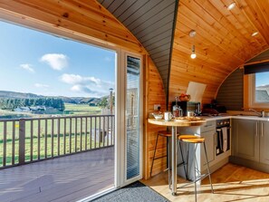 A wooden interior with a kitchen and a balcony overlooking a rural landscape.
