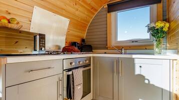 Une cuisine compacte équipée d’une cuisinière, d’un four et d’un évier, avec un plafond en bois et une fenêtre offrant une vue agréable.