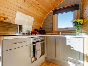 A compact kitchen with a stove, oven, and sink, wooden ceiling, and a window with a view.
