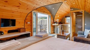 A cozy cabin interior with a bed, a TV, a dining area, and a bathroom.