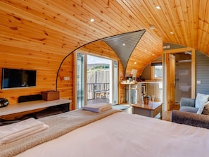 A cozy cabin interior with a bed, a TV, a dining area, and a bathroom.