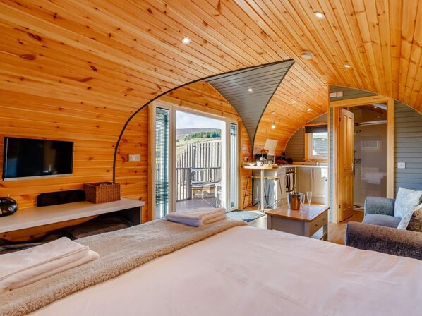 A cozy cabin interior with a bed, a TV, a dining area, and a bathroom.