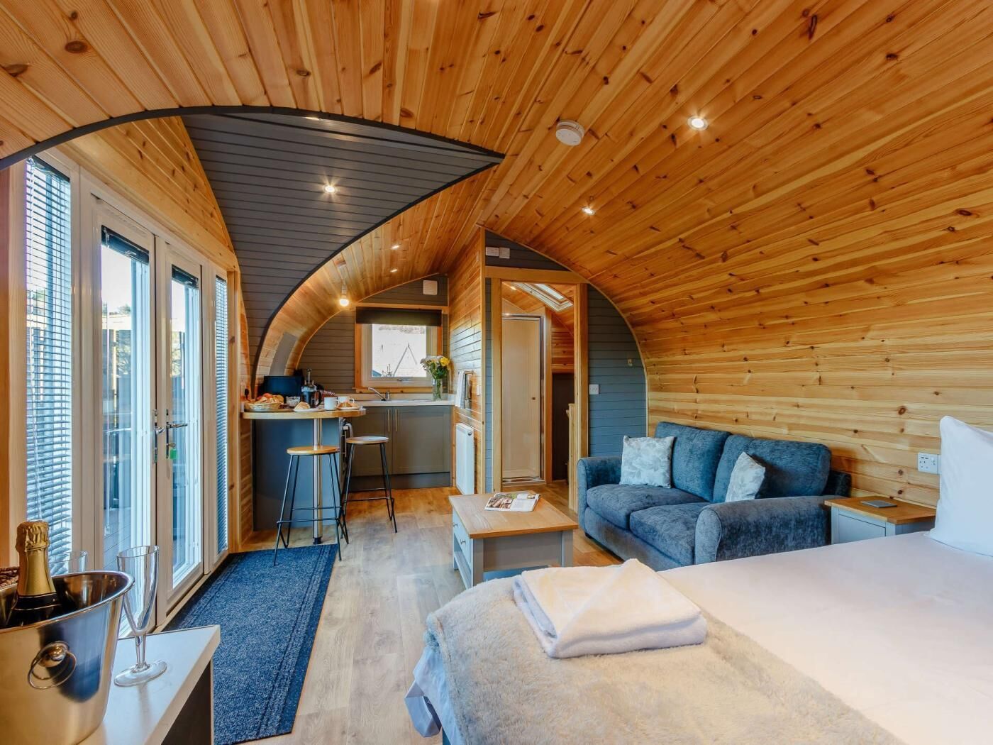 Una cabaña acogedora de techo curvo con kitchenette, un sofá y una cama.