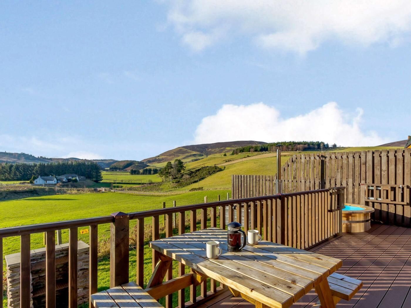 Une terrasse en bois avec une table et des chaises, un jacuzzi et une vue sur des collines ondoyantes.