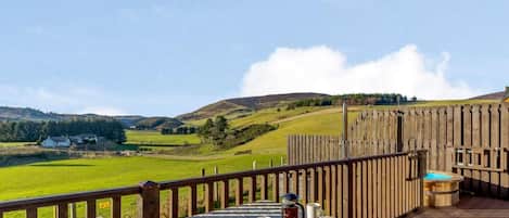 A wooden deck with a table and chairs, a hot tub, and a view of rolling hills.