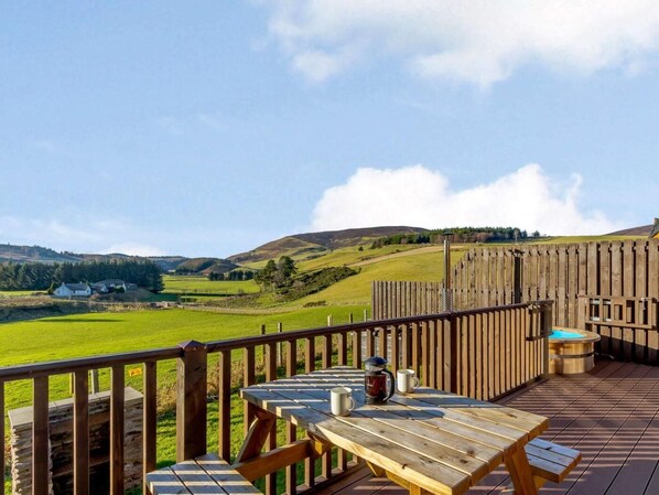 A wooden deck with a table and chairs, a hot tub, and a view of rolling hills.