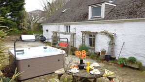 Ein Whirlpool, ein Holztisch und Stühle in einem Gartenbereich mit einem weißen Haus im Hintergrund.