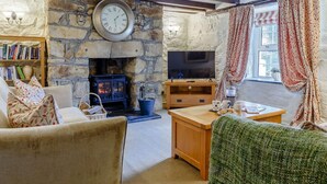 Ein gemütliches Wohnzimmer mit Kamin aus Stein, einem Fernseher und einem Bücherregal.