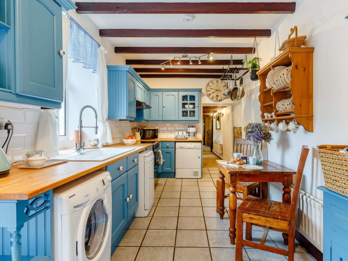 A kitchen with blue cabinets, a wooden table, and a hanging clock.