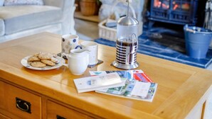 Ein Holztisch mit einem Teller Keksen, zwei weiße Tassen mit blauen Punkten und einer silbernen Kaffeekanne sowie einigen Papieren.