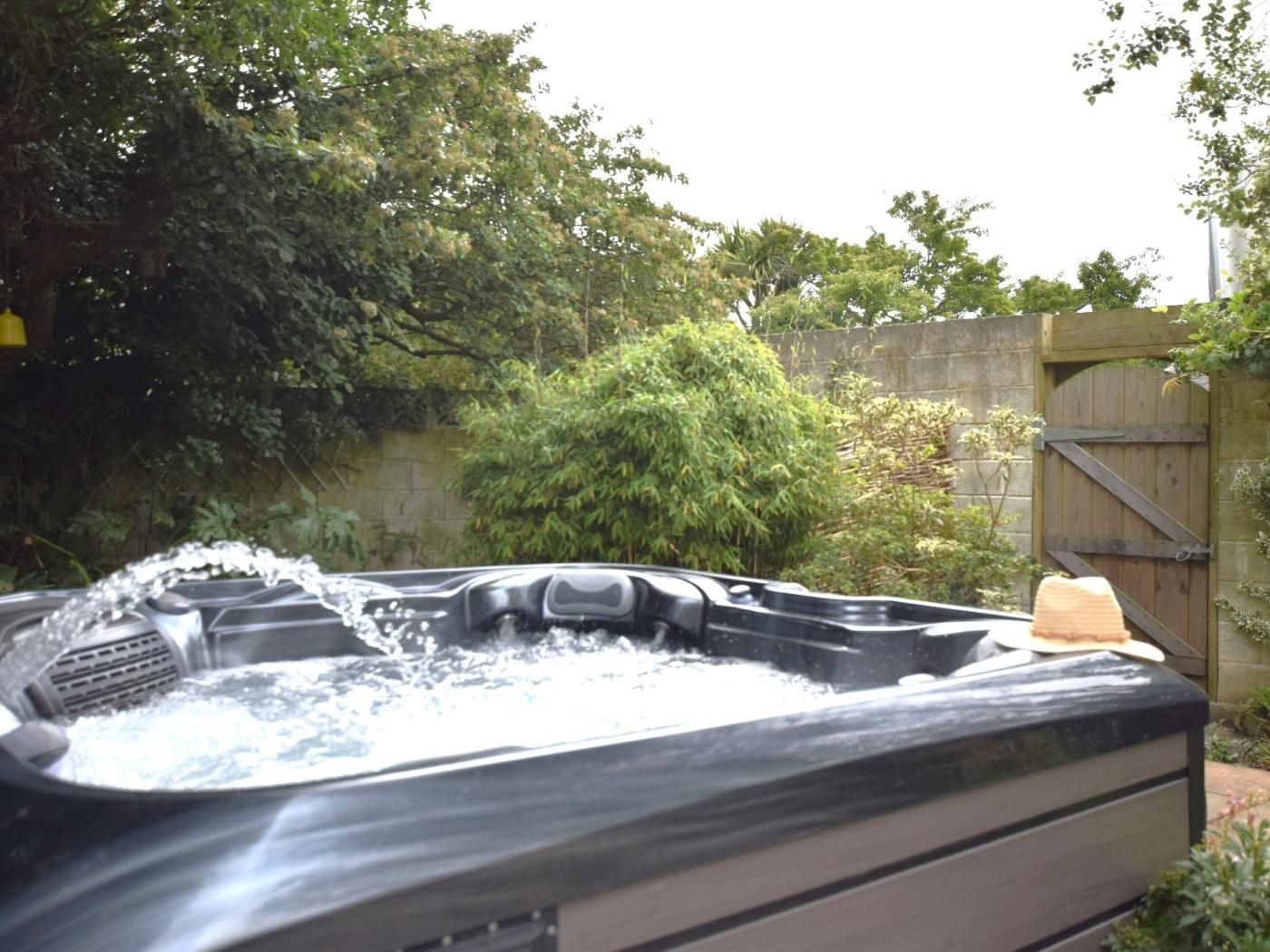 Un jacuzzi con chorros de agua, rodeado de follaje y una valla de madera.