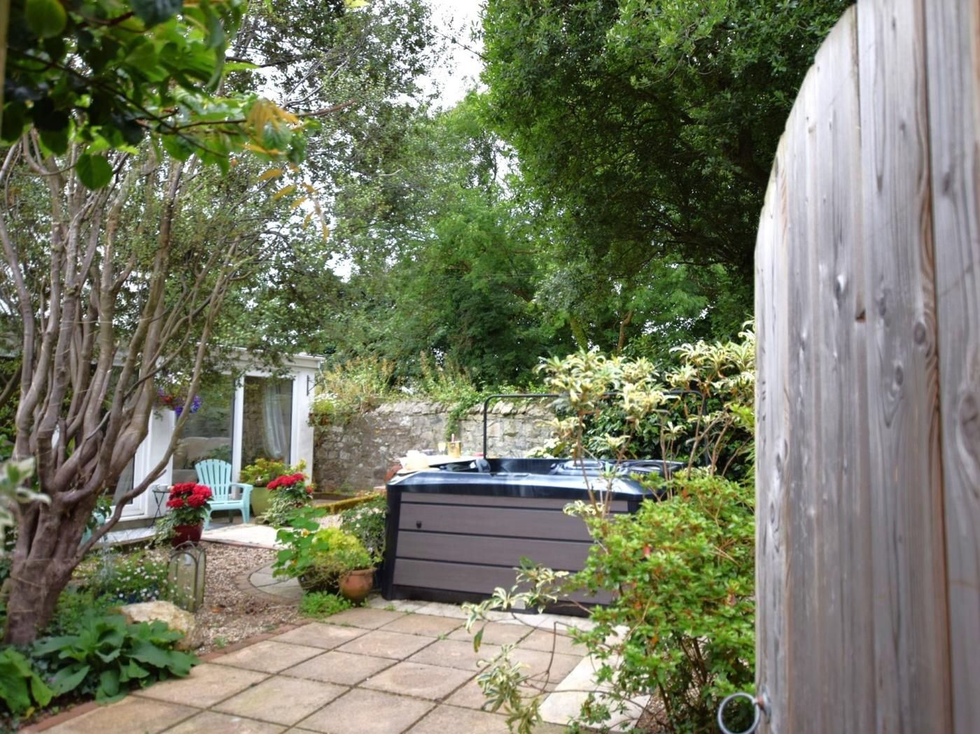 A garden with a hot tub, a stone wall, and a variety of plants.