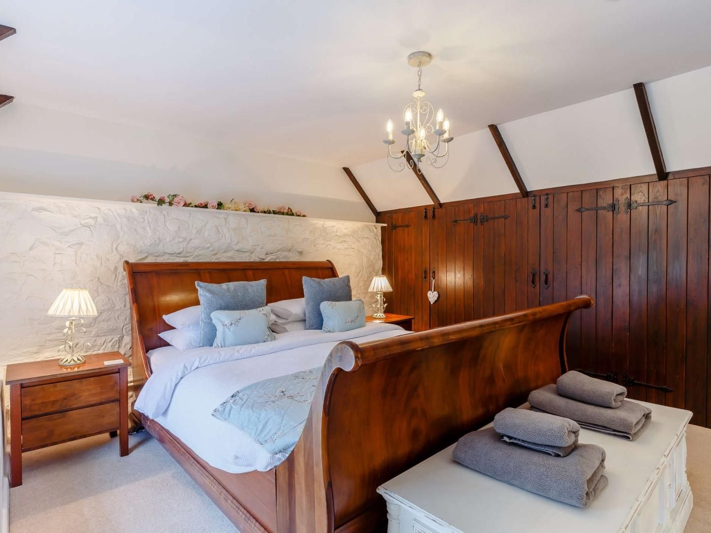 Quarto com cama de madeira, mesas de cabeceira, um lustre e um guarda-roupa.
