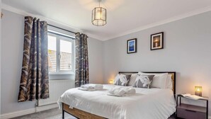 Ein Schlafzimmer mit Bett, Nachttisch, einem Fenster mit Vorhängen und einer Deckenleuchte.