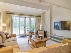 Ein Wohnzimmer mit einer Couch, einem Couchtisch und einem Kamin. Ein Fernseher ist an der Wand montiert und eine Glastür führt in einen Garten.