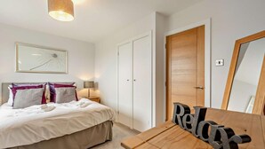 A bedroom with a bed, bedside lamp, wooden dresser, mirror, and a framed picture on the wall. - 2 Bed in Woolacombe (oc-westd) (Woolacombe)