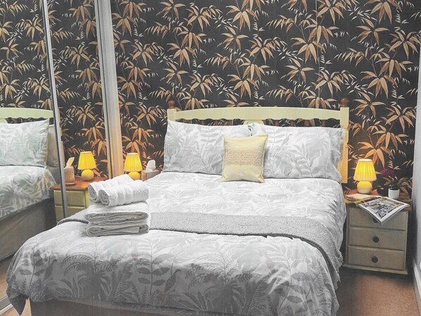 Ein Schlafzimmer mit einem Bett, zwei Nachttischen, einem Spiegel und einer Wand mit Muster.