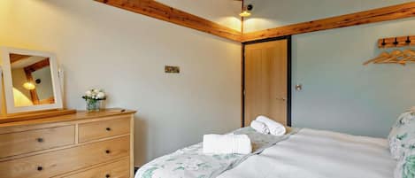 A bedroom with a wooden ceiling, a bed with floral bedding, a dresser, a mirror, and a door.