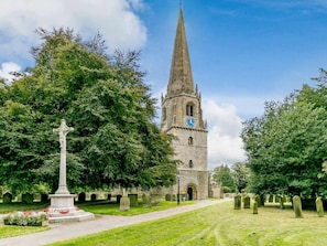 Eine Kirche mit einem hohen Kirchturm, einem Kreuzdenkmal und einem Friedhof mit Grabsteinen.