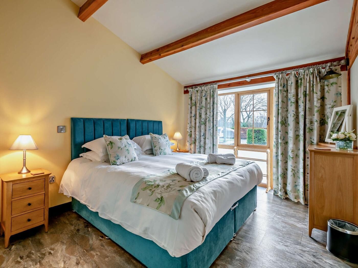 A bedroom with a bed, nightstands, a dresser, and a window with curtains.