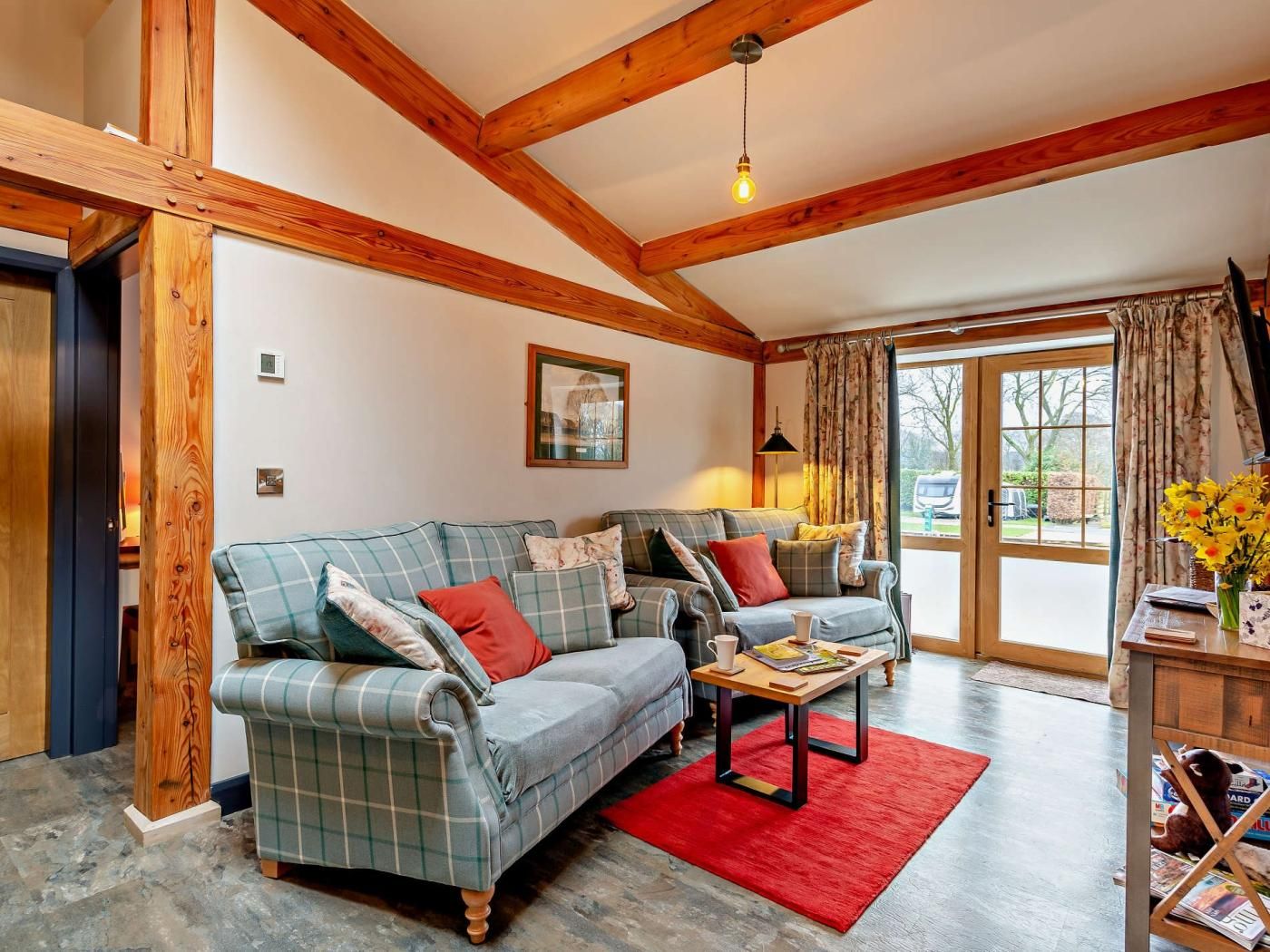 A living room with a plaid sofa, a red rug, and a wooden ceiling.