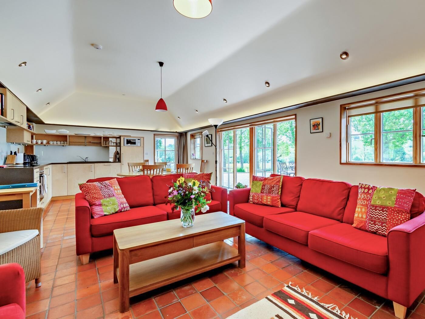 A spacious living area with a red sofa set, a wooden coffee table, and a kitchen in the background.