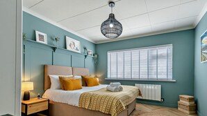 Ein Schlafzimmer mit einem Bett, Nachttischen, einer Lampe, einem Heizkörper, einem Fenster mit Jalousien und einer Pendelleuchte.