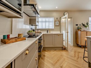 A modern kitchen with a herringbone floor pattern, a built-in oven, and a large island with a bowl of fruit. - 3 Bed in Aberaeron (oc-88788) (Aberarth)