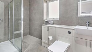 Een moderne badkamer met een douchecabine van glas, een wastafel met spiegel en een toilet.