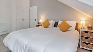 Een slaapkamer met een groot bed, twee nachtkastjes met lampen, een kledingkast en een deur.