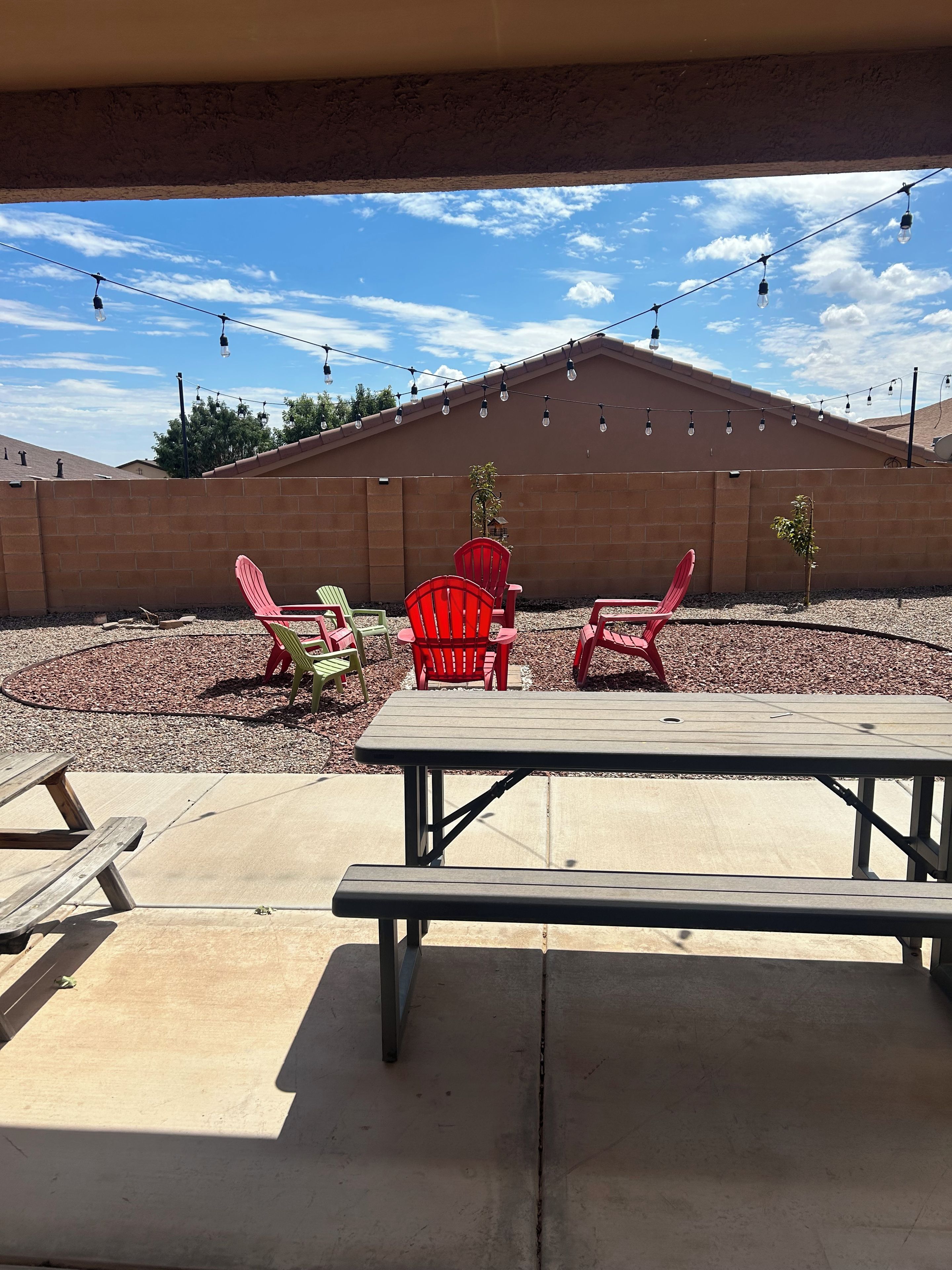 An outdoor patio with a picnic table and red chairs, a brick wall, and string lights.